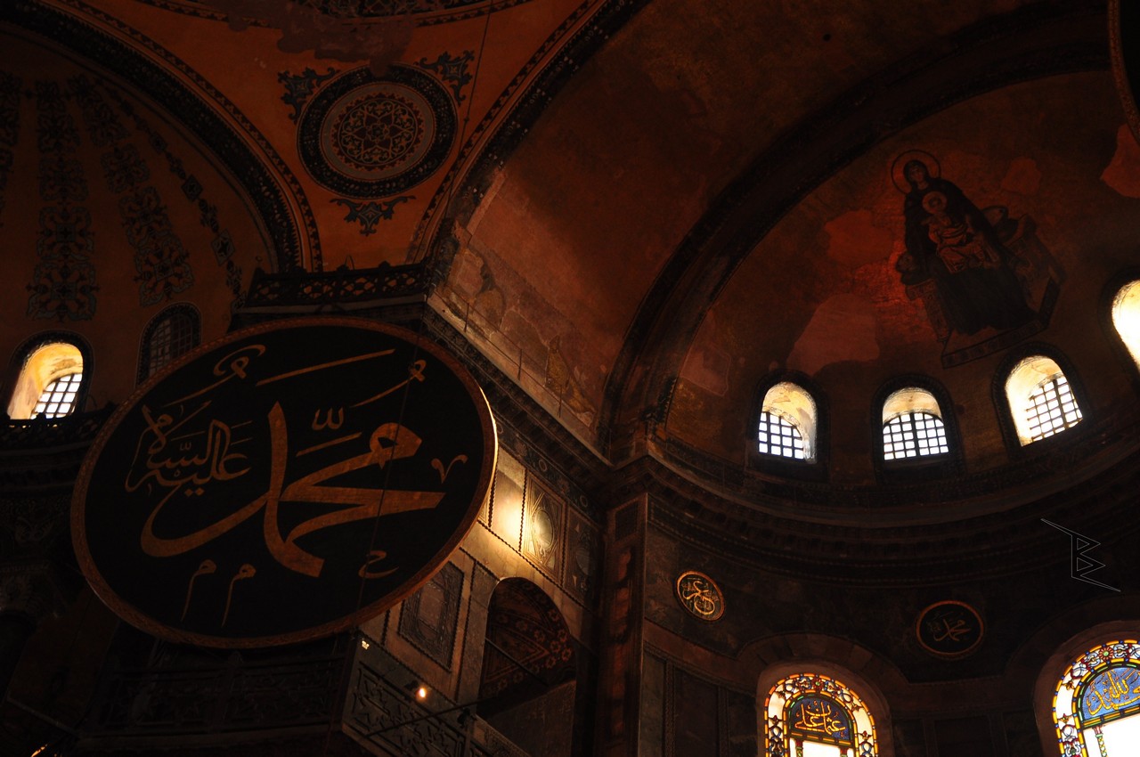 A Hagia Sophia interior photo showing a large calligraphic medallion, arched ceiling and warm windows.