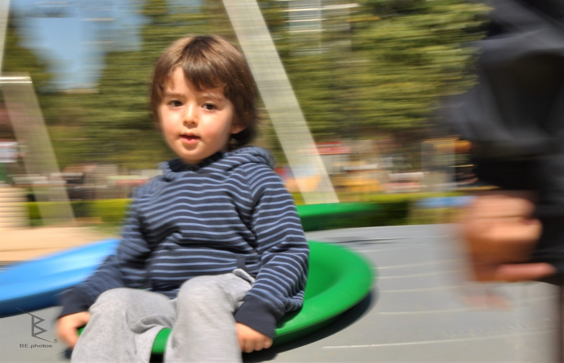Panning photography of a child looking toward the camera while a colorful playground spins into motion blur behind him.