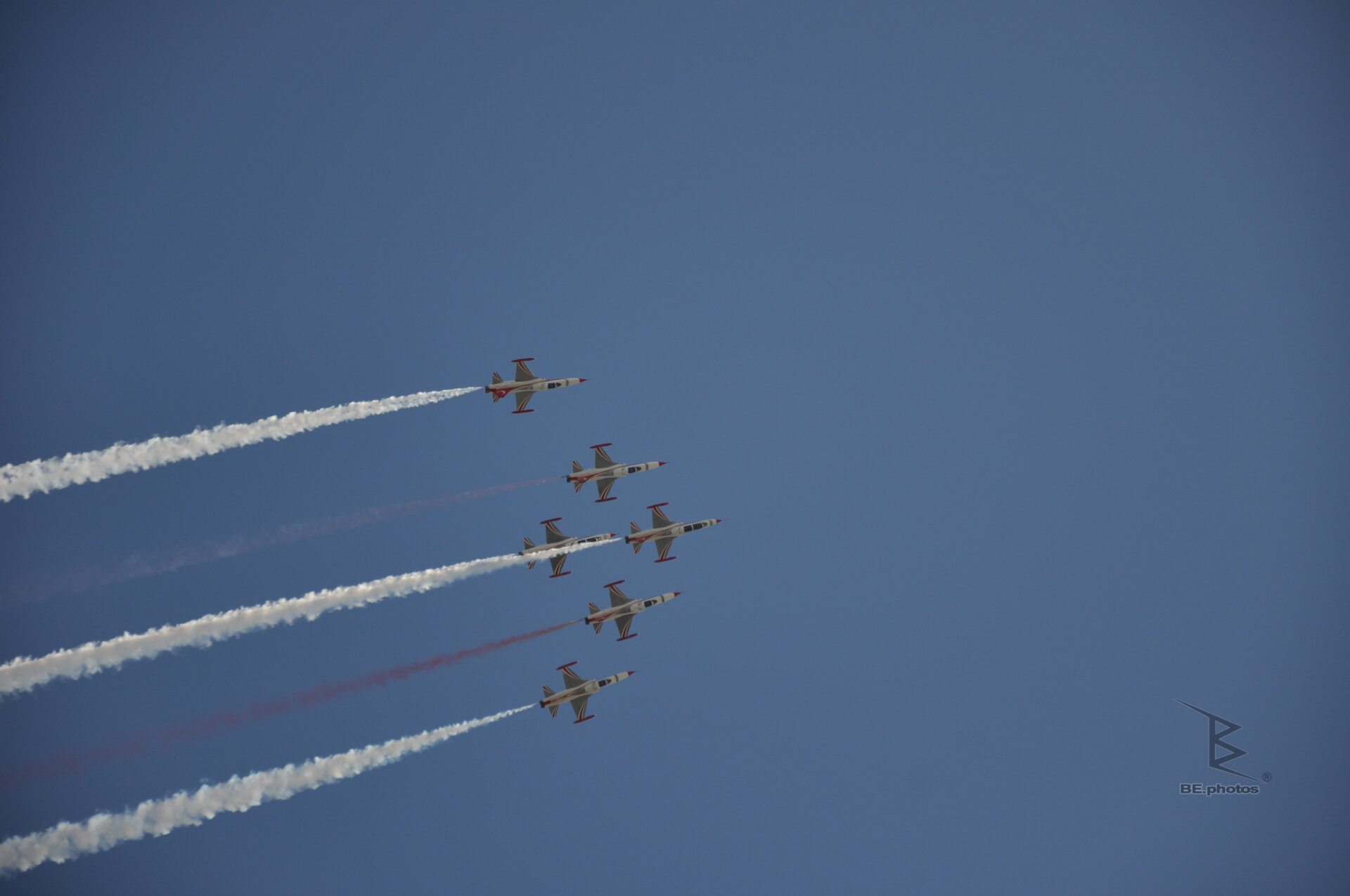 Turkish Stars jets flying in formation with white and red smoke trails across a blue sky.