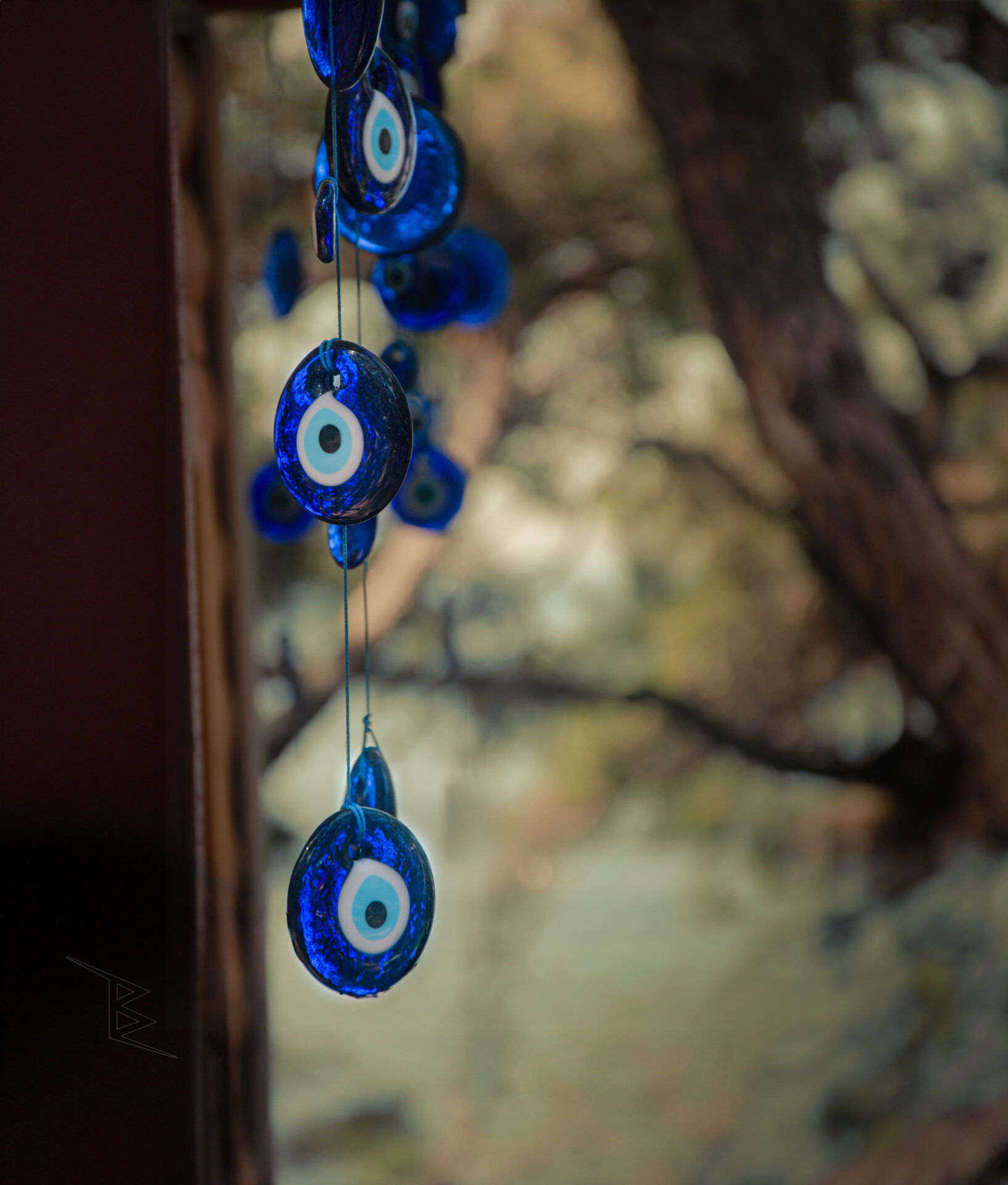 Several blue Turkish evil eye beads hanging in front of a softly blurred outdoor background.