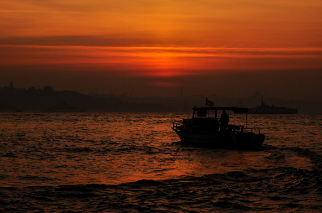Boat at sunset photo of a small boat crossing dark, rippling water beneath layered orange and red light.